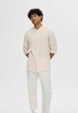 Camisa de botón de manga larga en rosa claro con collar mao y sutiles rayas verticales; combinada con pantalones blancos.