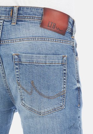 Jean en denim bleu clair avec une étiquette en cuir marron à la taille, comportant des accents de couture et un design de poche arrière visible.