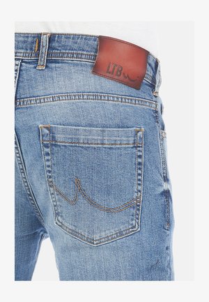 Light blue denim jeans with a brown leather label at the waistband, featuring stitching accents and a visible back pocket design.