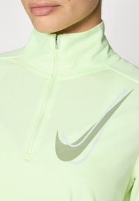Light green zip-up athletic top made of soft fabric. Features a stand-up collar and a dynamic swoosh logo in dark and light shades.
