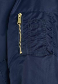 Tessuto della giacca blu navy con una zip dorata visibile e una tasca applicata con cuciture orizzontali. Texture liscia e design semplice.