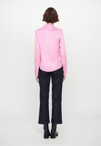 Pink long-sleeve shirt with a textured pattern, curved hem, and collar, paired with dark denim flared pants and black ankle boots.