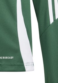 Zelena sportska majica s bijelim akcentima i tri vertikalne pruge na ramenima. Izrađena od teksturirane tkanine; sadrži "AEROREADY" marku.