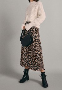 Dikke crème gebreide trui, lange bruine rok met luipaardprint, zwarte schoudertas en zwarte veterschoenen.