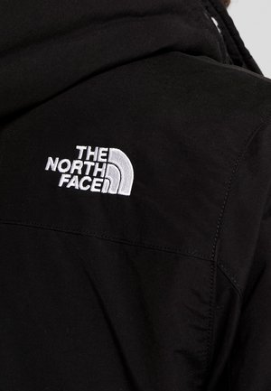 Czarna kurtka z białym, haftowanym logo „The North Face” na górnej części pleców, w pobliżu szwu barkowego.