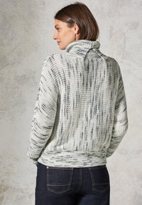 Chunky gebreide trui in wit en grijs met een hoge kraag, voorzien van een textuurpatroon en geribde manchetten. Gekoeld met donkere jeans.