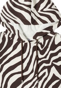 Sweat à capuche avec des rayures zébrées noires et blanches et des cordons marron avec embouts métalliques.