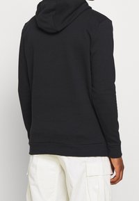 Sweat à capuche noir avec manches longues et poignets côtelés. Tissu doux à texture lisse, doté d'une poche kangourou et d'une coupe décontractée.