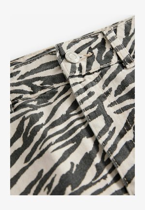 Tkanina s zebrovaným vzorom s čiernymi a slonovinovými pruhmi, so zapínaním na kovový gombík a viditeľnými švami. Textúrovaný, odolný denimový materiál.