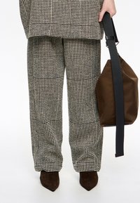 Szerokie spodnie w czarno-białym wzorze psiej zęby, zestawione z brązowymi butami w szpic i brązową torebką.