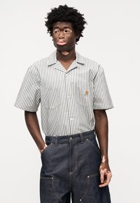 Πουκάμισο με κοντά μανίκια και γιακά σε μπλε και λευκές ρίγες, σε συνδυασμό με παντελόνι από σκούρο τζιν με μεγάλες τσέπες και αντίθετες ραφές.