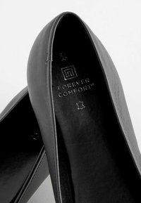 Ballerine nere in finta pelle con una texture liscia, punta arrotondata e dettagli di cucitura sottili. Presentano il marchio "Forever Comfort" all'interno.