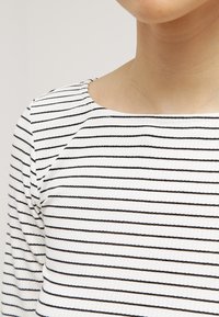 Bílý pruhovaný top s horizontálními černými pruhy, s kulatým výstřihem a těsnými rukávy. Minimalistický design s texturovanou látkou.