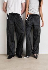 Black, loose-fitting cargo pants in shiny material with an elastic waistband, front pockets, and subtle texture details. Casual design.