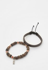 Due braccialetti: uno è un bracciale in pelle marrone, l'altro presenta perline di legno con accenti rossi e bianchi, con un'etichetta metallica attaccata.