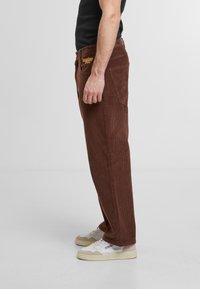Brown corduroy pants with a straight-leg design, featuring front and back pockets and orange embroidered logo on the waistband.