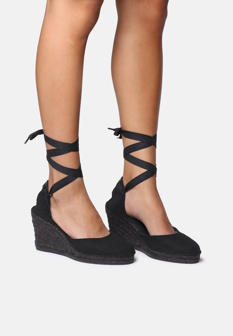 Espadrillas nere a zeppa con suola intrecciata texturizzata. Presentano lacci incrociati alla caviglia e una parte superiore in tela liscia. Design con tallone aperto.