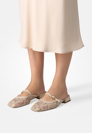 Beige Häkelschuh-Mules mit flachen Blockabsätzen und einem kleinen Riemen mit Schnalle, getragen zu einem cremefarbenen Midirock.