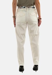 Pantalons blancs taille haute avec une texture lisse, dotés de deux poches arrière et d'une taille ajustée. Associés à des chaussures à talons hauts noires.