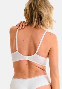 Witte beha met verstelbare bandjes en haaksluiting. De achterkant heeft een gladde afwerking met geschulpte kantafwerking. Zachte stof, minimale stijl.