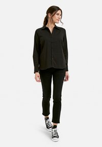Black button-up shirt with a collar, long sleeves, and a relaxed fit, paired with black slim jeans and black and white sneakers.