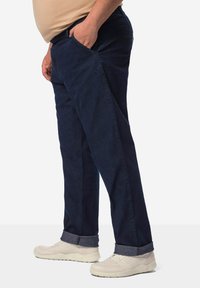 Pantalones de mezclilla azul oscuro con un diseño de pierna recta, que presentan bolsillos laterales y puños enrollados, combinados con zapatillas deportivas de color claro.