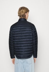 Giacca trapuntata blu navy realizzata in materiale leggero. Presenta un colletto alta e un orlo arrotondato, con cuciture visibili e una finitura liscia.
