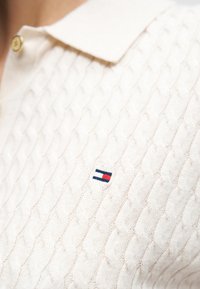 Πλεκτό πόλο σε κρεμ χρώμα με υφή πλεξίματος σε μοτίβο καλώδιου. Διαθέτει μικρό κεντημένο λογότυπο με κόκκινες, λευκές και μπλε λεπτομέρειες. Λεπτομέρειες με χρυσά κουμπιά.