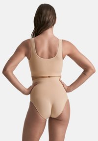 Completo sportivo beige composto da un reggiseno a scollo rotondo e pantaloni corti a vita alta. Tessuto morbido con cuciture minime e dettagli del logo sul retro.