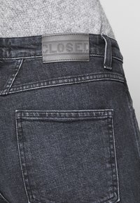 Jeans de denim oscuro con un parche de cuero con la marca "CLOSED", diseño clásico de cinco bolsillos y costuras en contraste.