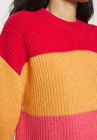 Strickpullover mit horizontalen Streifen in Rot, Orange und Pink. Gerippte Textur am Kragen und weiche Webart insgesamt.