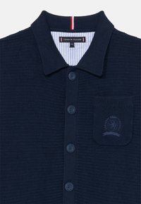 Marineblaues Strick-Polohemd aus strukturiertem Stoff, ausgestattet mit einem Kragen, sechs Knöpfen und einer gestickten Tasche mit einem Emblemdetail.