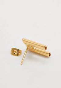 Gold-toned metal earring post lying on a white surface with a separate matching back clasp visible beside it.