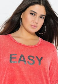 Rood oversized t-shirt met een relaxte pasvorm, voorzien van een ronde hals en het woord "EASY" in zwarte vette letters over de voorkant.