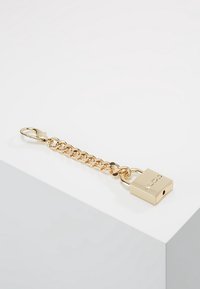 Guld kedjehängare med ett litet hänglås med ett nyckelhål och en graverad logotyp, som visar en slät metallisk finish och kedjad design.