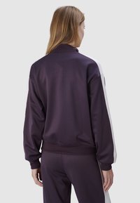 Paarse trainingsjack met een hoge kraag, geribde manchet en witte zijpanelen. Soepele textuur, relaxte pasvorm, geschikt voor sportkleding.