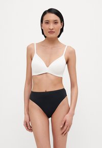 White molded bra with thin straps and a V-neck design, paired with high-waisted black bikini bottoms, both featuring smooth fabric.