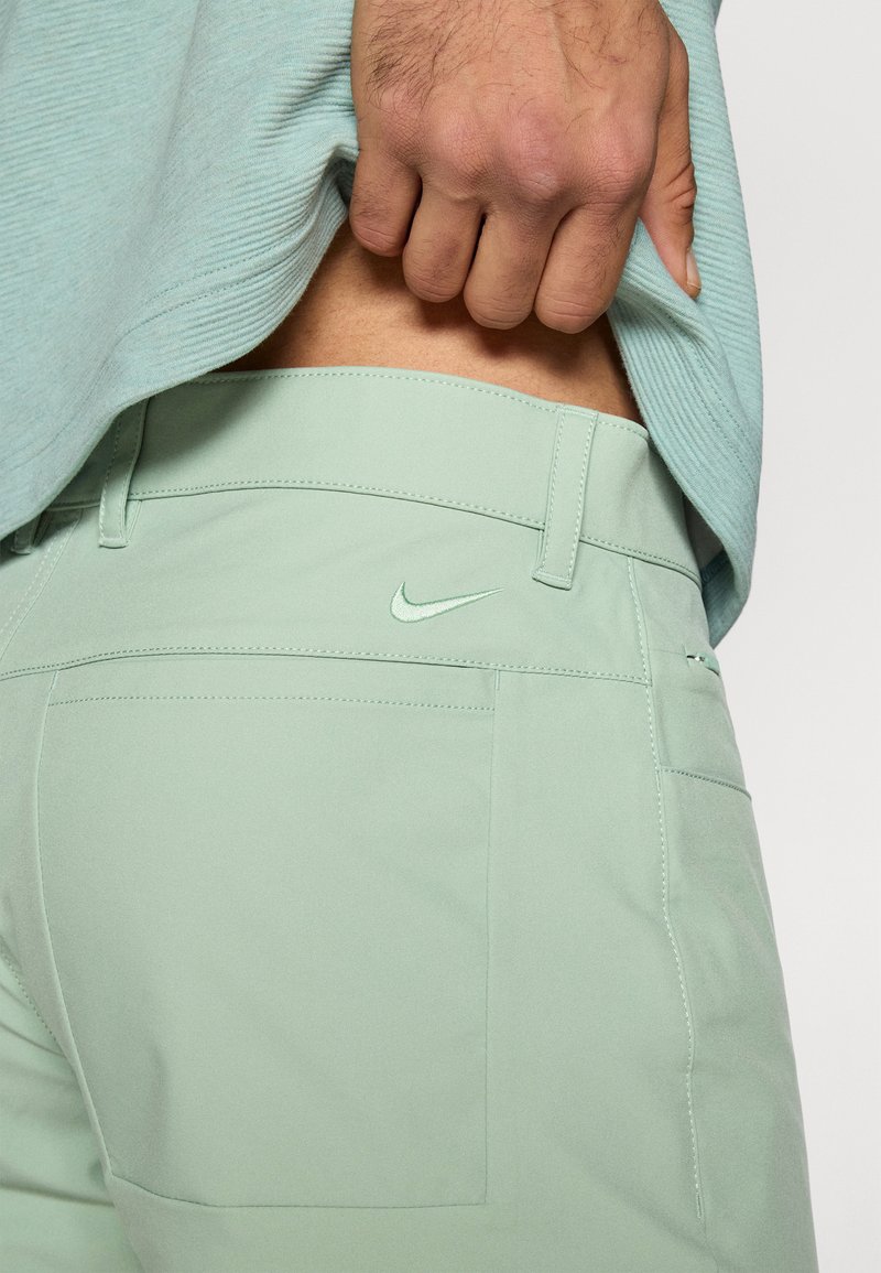 Lichtgroene Nike-broek van een gladde, lichte stof, met een klein logo op de achterzak en subtiele stikdetails.