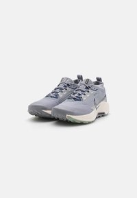 Scarpe da ginnastica grigio chiaro con una parte superiore testurizzata, dettagli blu navy e una suola bianca spessa. Presentano un punta rinforzata e lacci flessibili.