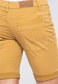 Shorts en coton jaune avec un ourlet roulé, comprenant des poches arrière et des détails de couture subtils. Étiquette de la marque sur la taille.