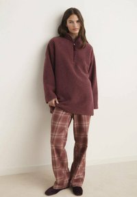 Sudadera de forro polar burdeos con cuello de media cremallera, combinada con pantalones de cuadros en tonos burdeos y beige, con un corte relajado.