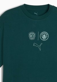 Camiseta de algodón verde oscuro con los logotipos de EA Sports Football Club y Manchester City. Mangas cortas, cuello redondo y textura sutil.