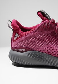 Les sneakers Adidas AlphaBounce disposent d'un supérieur en mesh texturé fuchsia avec une semelle grise rembourrée, des lacets contrastants et un onglet de talon de soutien.