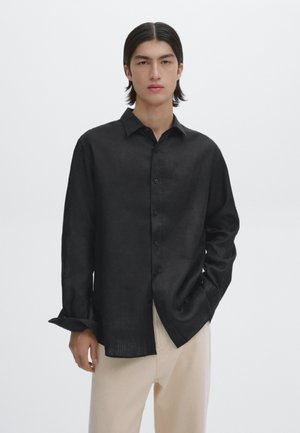 Black button-up shirt made of lightweight fabric, featuring a classic collar, long sleeves, and a relaxed fit. Worn with light-colored trousers.