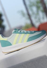 Hellblauer und gelber Sneaker mit weißen Schnürsenkeln, der auf einer weißen Oberfläche vor einem verschwommenen Außenhintergrund liegt.
