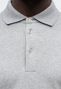 Tricou polo gri cu guler, având trei butoane și un material texturat. Include un detaliu de buzunar pe pieptul stâng.