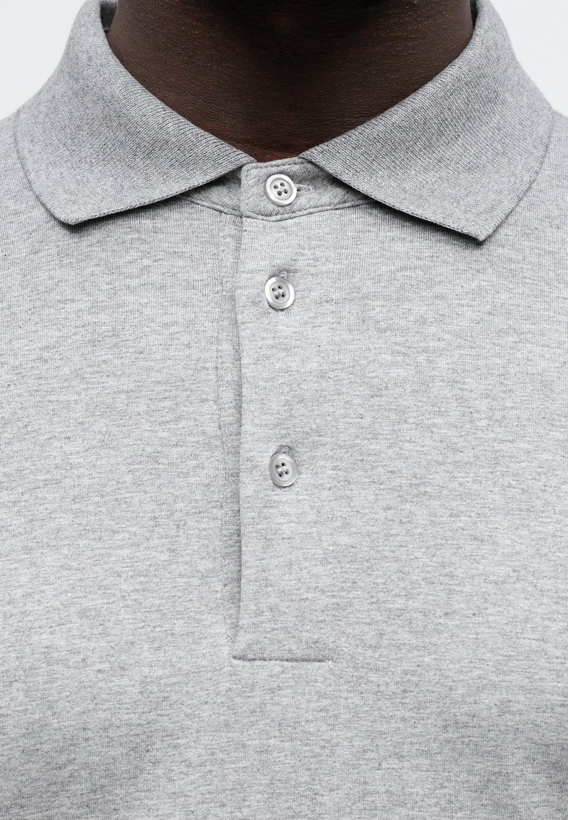 Polo grigio con colletto, dotato di tre bottoni e un tessuto testurizzato. Include un taschino sul lato sinistro del petto.