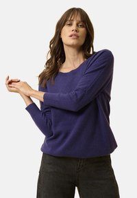 Maglione di lana viola con maniche lunghe, vestibilità leggermente oversize, scollatura ampia e texture morbida, abbinato a jeans scuri.