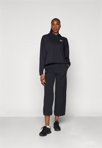 Sudadera negra corta con un logo en el pecho, combinada con pantalones cargo negros holgados que tienen bolsillos laterales y puños elásticos. Zapatillas negras.