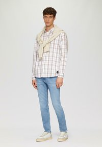 Chemise à carreaux blanche, marron et crème ; jeans bleu clair ; pull crème noué autour du cou ; baskets ivoire.